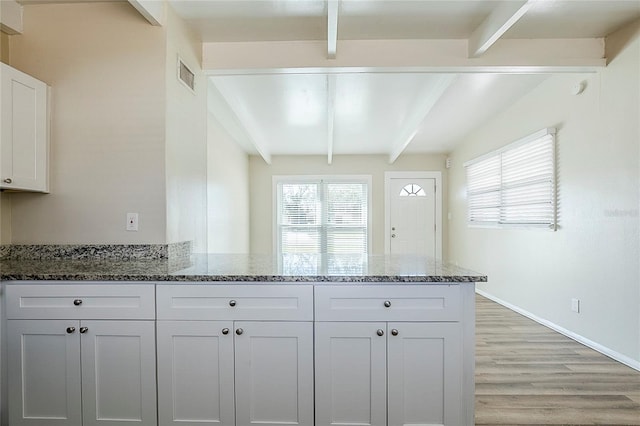 kitchen with stone counters, beamed ceiling, and a peninsula