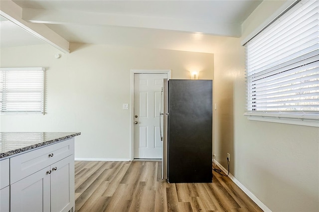 kitchen featuring baseboards, light wood-style floors, freestanding refrigerator, stone counters, and white cabinetry