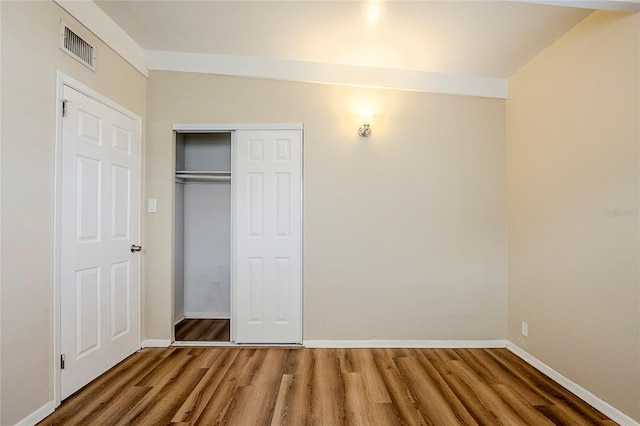 unfurnished bedroom featuring a closet, visible vents, baseboards, and wood finished floors