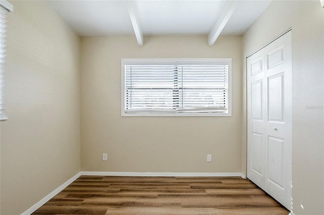 unfurnished bedroom with beamed ceiling, wood finished floors, and baseboards