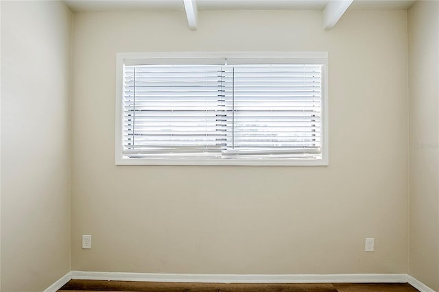 spare room with beam ceiling, a wealth of natural light, and baseboards