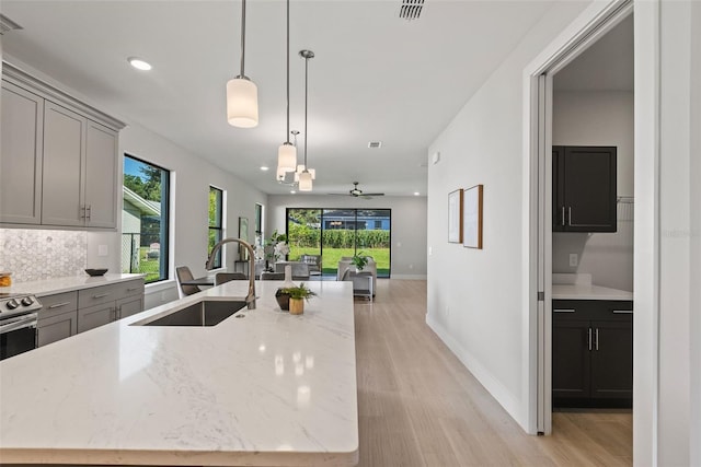 kitchen with sink, gray cabinets, light stone countertops, and a center island with sink