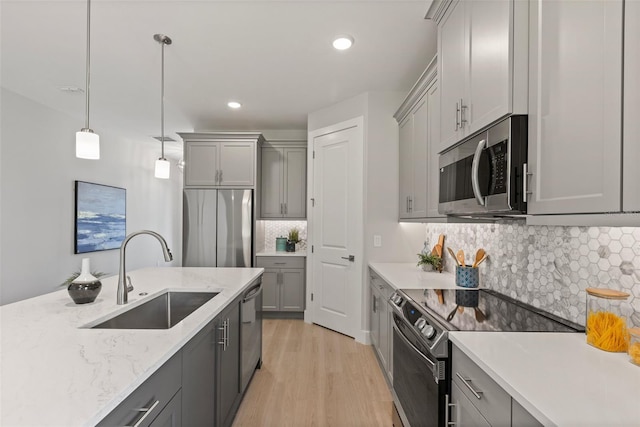 kitchen with sink, gray cabinetry, decorative light fixtures, appliances with stainless steel finishes, and light hardwood / wood-style floors