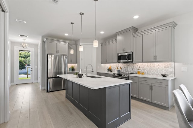 kitchen featuring sink, gray cabinetry, hanging light fixtures, stainless steel appliances, and a center island with sink