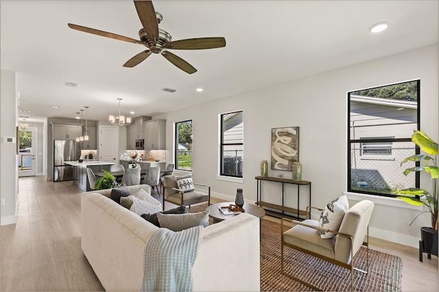 living room featuring ceiling fan with notable chandelier and light wood-type flooring