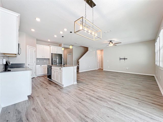 kitchen with appliances with stainless steel finishes, an island with sink, white cabinets, decorative light fixtures, and light wood-type flooring