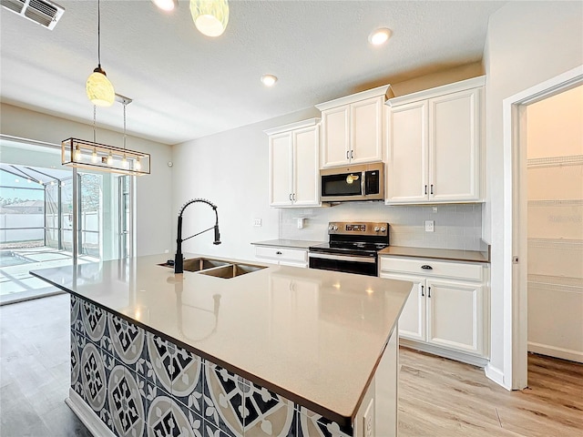 kitchen featuring sink, a kitchen island with sink, white cabinetry, stainless steel appliances, and decorative light fixtures