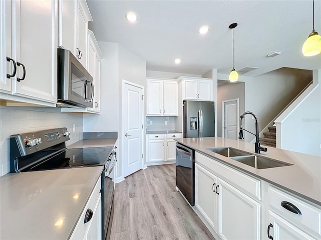 kitchen with appliances with stainless steel finishes, sink, pendant lighting, and white cabinets