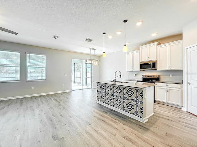 kitchen with decorative light fixtures, an island with sink, sink, white cabinets, and stainless steel appliances