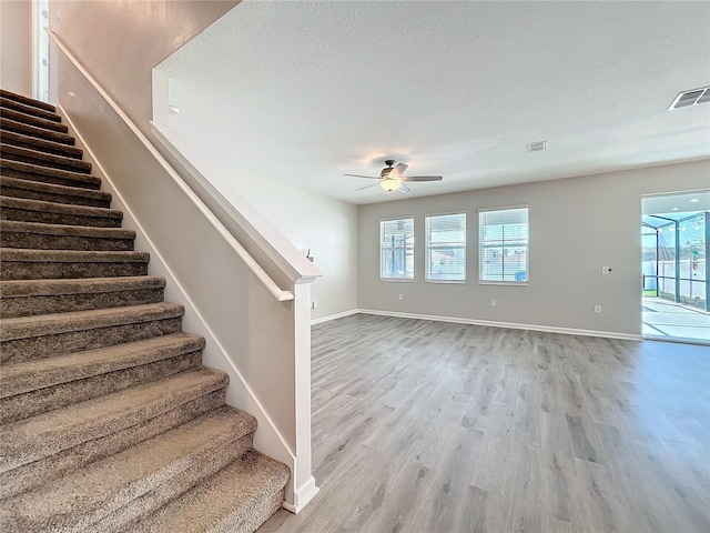 staircase featuring wood-type flooring, ceiling fan, and a textured ceiling