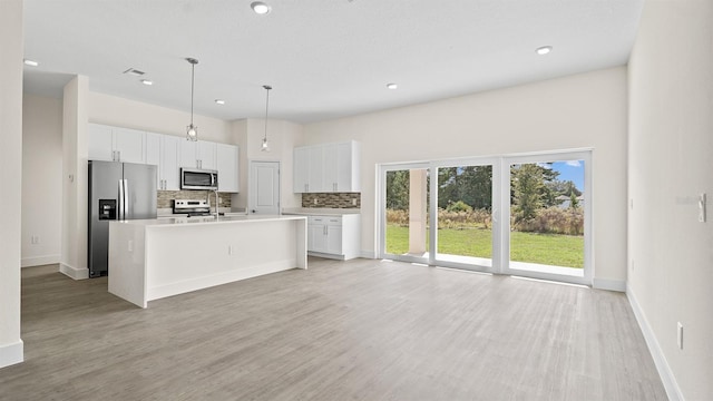 kitchen with pendant lighting, appliances with stainless steel finishes, white cabinetry, backsplash, and a center island with sink