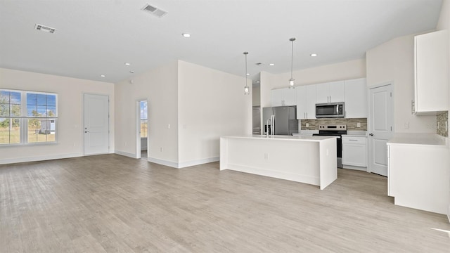 kitchen with a kitchen island, appliances with stainless steel finishes, white cabinets, decorative backsplash, and hanging light fixtures