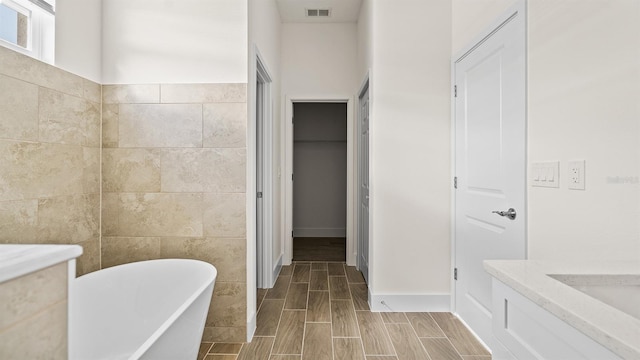 bathroom featuring a washtub, vanity, and tile walls