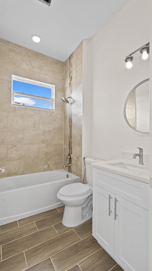 full bathroom featuring tiled shower / bath, vanity, and toilet