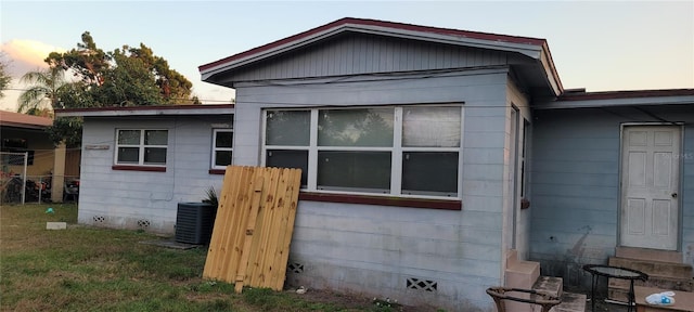 property exterior at dusk with cooling unit and a lawn