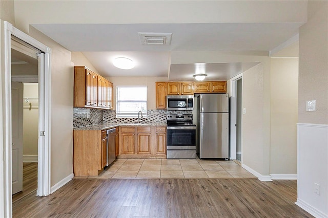 kitchen with stainless steel appliances, a sink, visible vents, light wood-style floors, and decorative backsplash