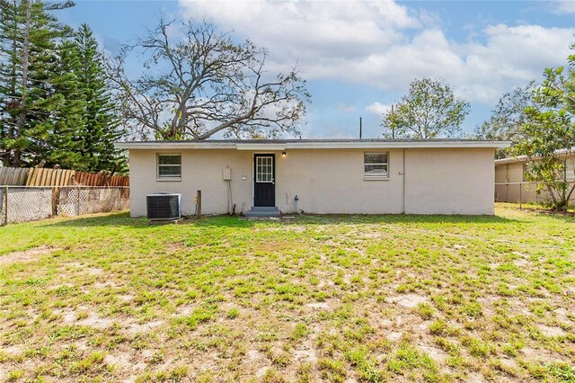 rear view of property featuring central AC unit, a lawn, a fenced backyard, and stucco siding