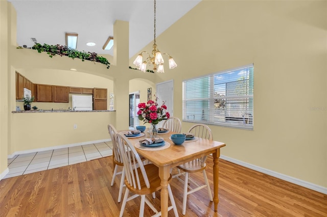 dining space featuring baseboards, arched walkways, a high ceiling, light wood-style floors, and a chandelier