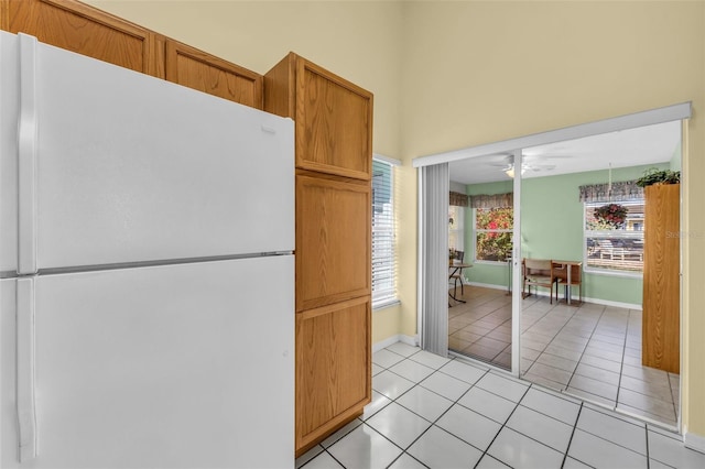 kitchen featuring light tile patterned floors, baseboards, a ceiling fan, brown cabinets, and freestanding refrigerator