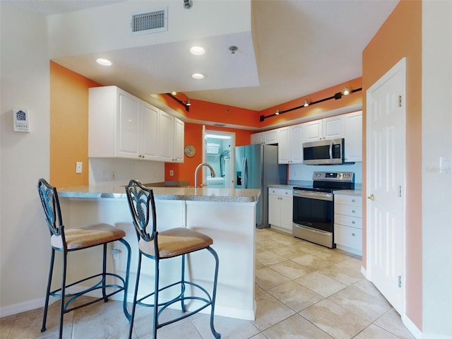 kitchen featuring stainless steel appliances, kitchen peninsula, a breakfast bar area, and white cabinets