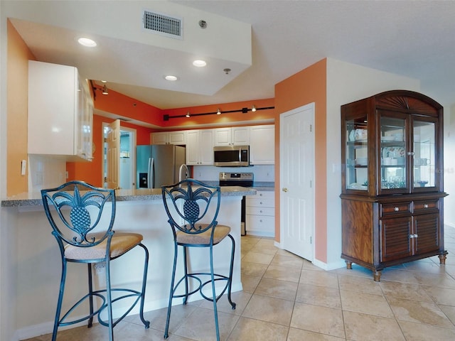 kitchen featuring appliances with stainless steel finishes, white cabinets, a kitchen bar, light tile patterned floors, and kitchen peninsula