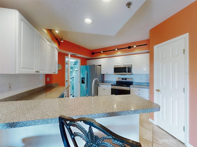 kitchen featuring light tile patterned floors, appliances with stainless steel finishes, white cabinets, a kitchen bar, and kitchen peninsula