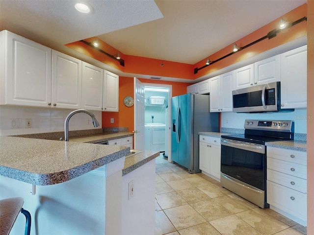 kitchen with a breakfast bar, appliances with stainless steel finishes, kitchen peninsula, a raised ceiling, and white cabinets