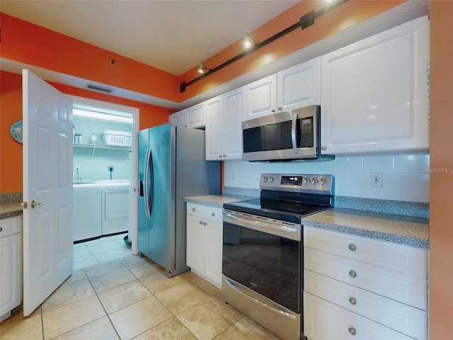 kitchen featuring light tile patterned flooring, appliances with stainless steel finishes, washer and dryer, and white cabinets