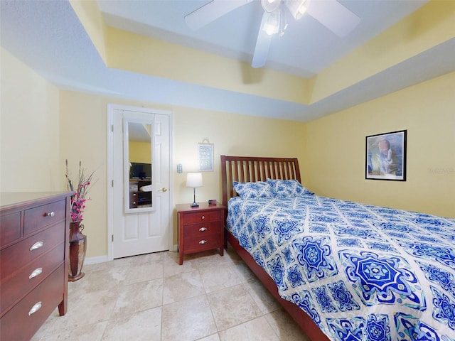 bedroom with light tile patterned floors, ceiling fan, and a tray ceiling