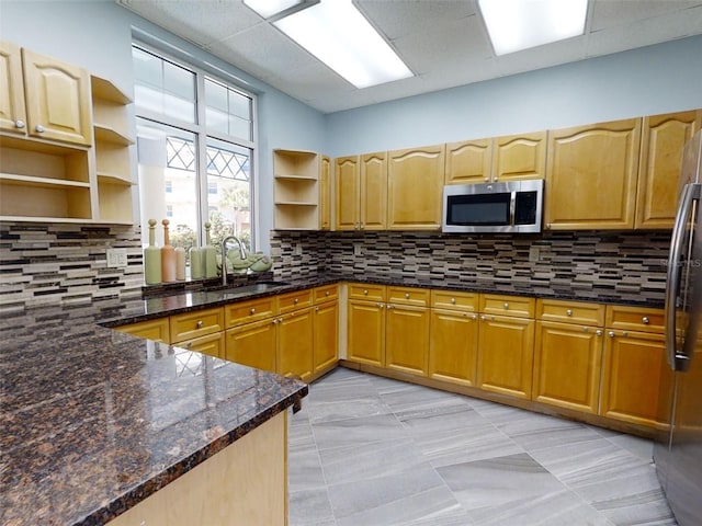 kitchen with appliances with stainless steel finishes, a paneled ceiling, sink, dark stone countertops, and backsplash