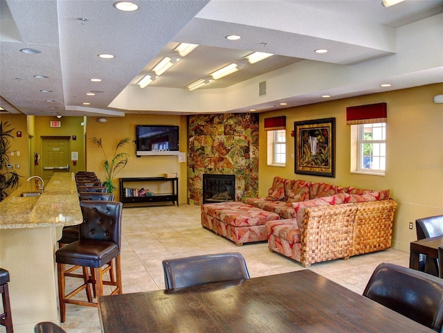 tiled living room featuring a large fireplace, sink, a textured ceiling, and a tray ceiling