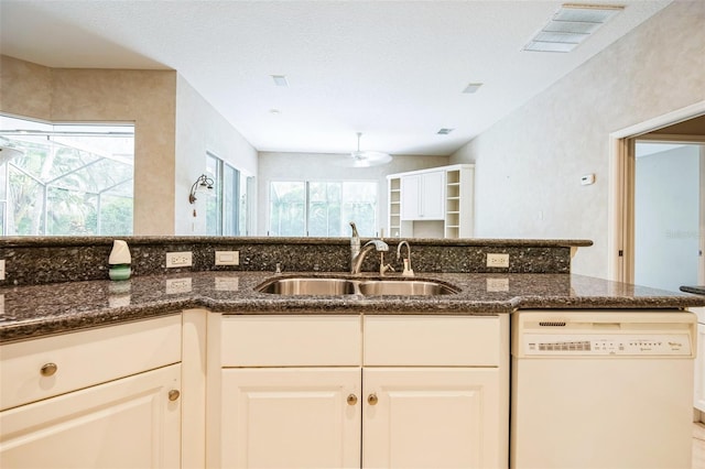 kitchen with white dishwasher, sink, dark stone counters, and white cabinets