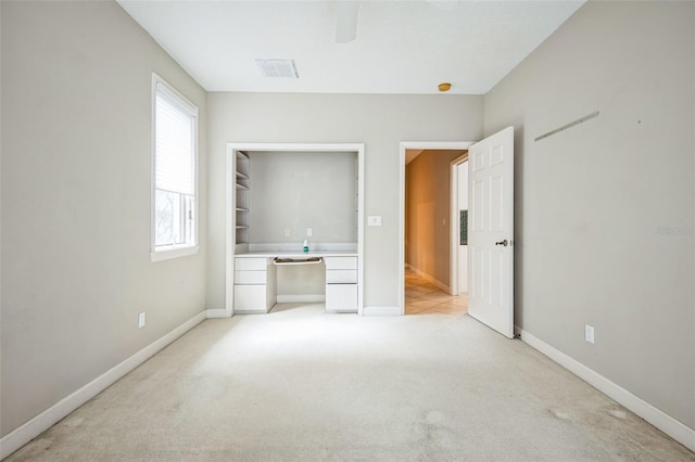 unfurnished bedroom with built in desk, light colored carpet, and ceiling fan