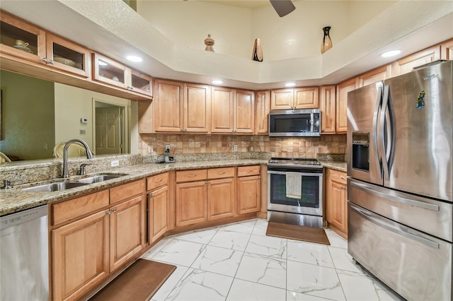 kitchen with tasteful backsplash, appliances with stainless steel finishes, sink, and light stone counters