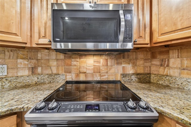 kitchen with appliances with stainless steel finishes, light stone counters, and decorative backsplash