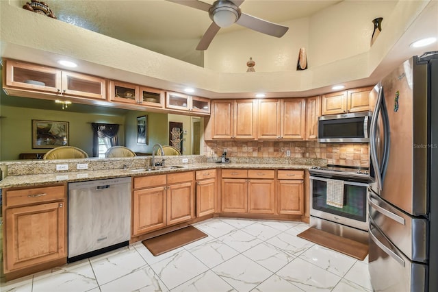 kitchen featuring sink, ceiling fan, stainless steel appliances, light stone counters, and decorative backsplash