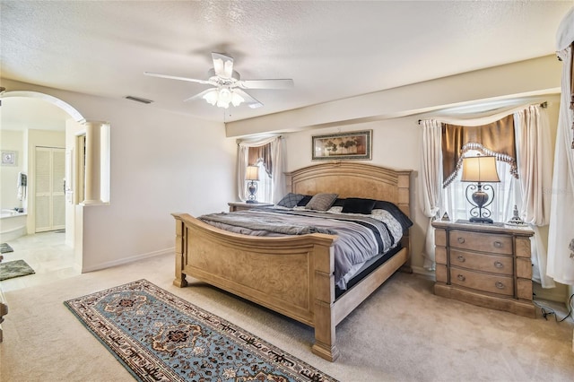 carpeted bedroom with ceiling fan, ensuite bathroom, a textured ceiling, and ornate columns