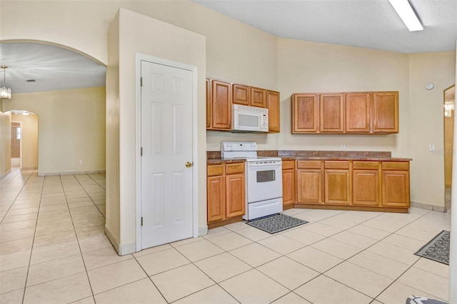 kitchen with decorative light fixtures, a high ceiling, light tile patterned floors, white appliances, and a textured ceiling