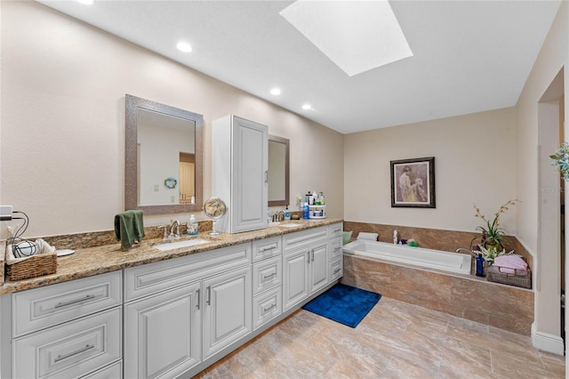 bathroom featuring vanity, tiled tub, and a skylight