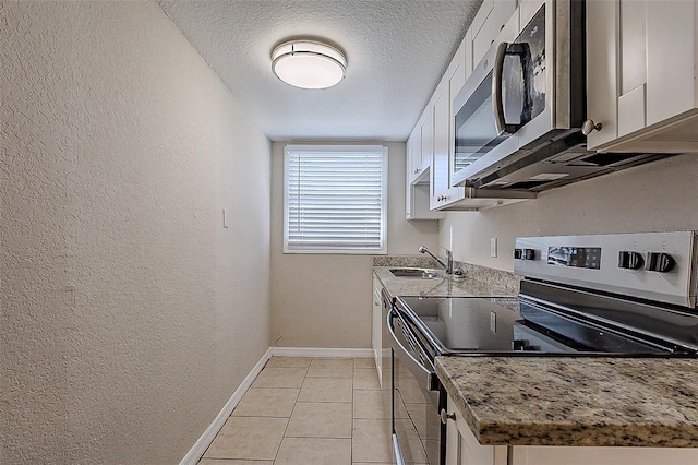 kitchen featuring appliances with stainless steel finishes, a sink, white cabinetry, and baseboards