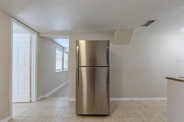 kitchen featuring baseboards, visible vents, a textured ceiling, and freestanding refrigerator