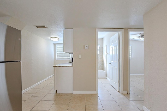 kitchen with light tile patterned floors, visible vents, white cabinets, freestanding refrigerator, and a textured ceiling