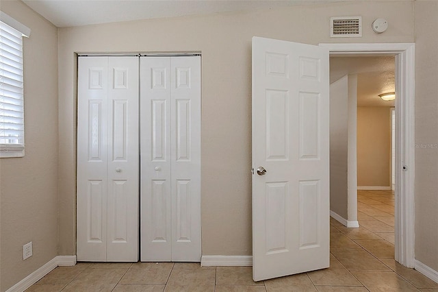 unfurnished bedroom featuring a closet, visible vents, baseboards, and light tile patterned floors