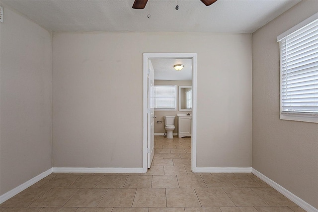 empty room with baseboards, a ceiling fan, and light tile patterned flooring