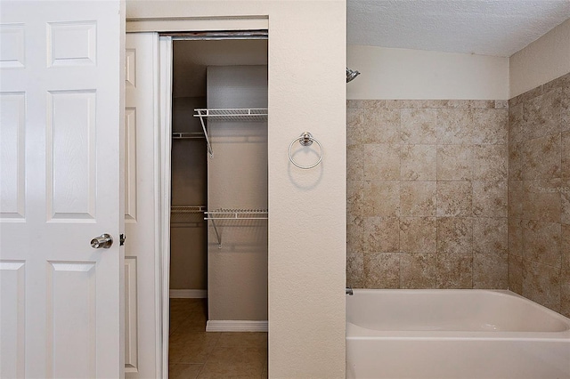 full bath with a walk in closet, a textured ceiling, baseboards, and tile patterned floors