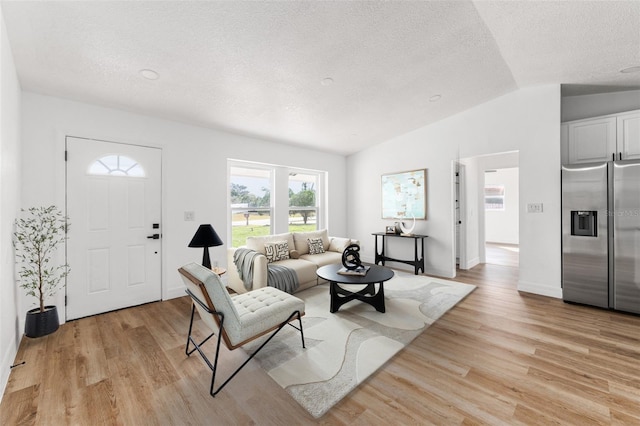 living room with vaulted ceiling, a textured ceiling, baseboards, and light wood-style floors