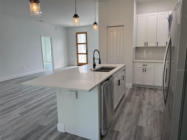 kitchen with a kitchen island with sink, a sink, wood finished floors, stainless steel appliances, and decorative backsplash