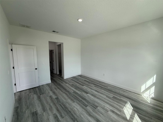 empty room with dark wood-type flooring, baseboards, visible vents, and a textured ceiling