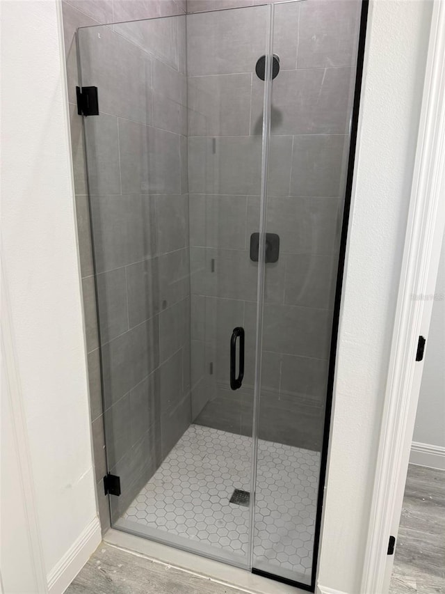 full bath featuring wood finished floors, baseboards, and a stall shower