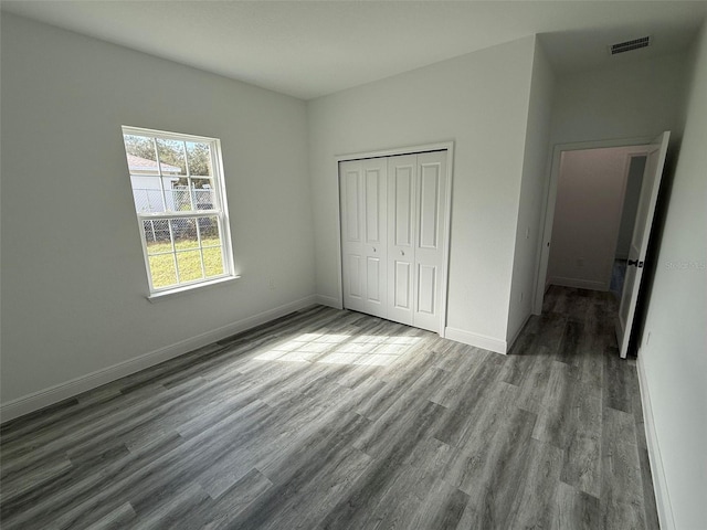 unfurnished bedroom featuring a closet, visible vents, baseboards, and wood finished floors